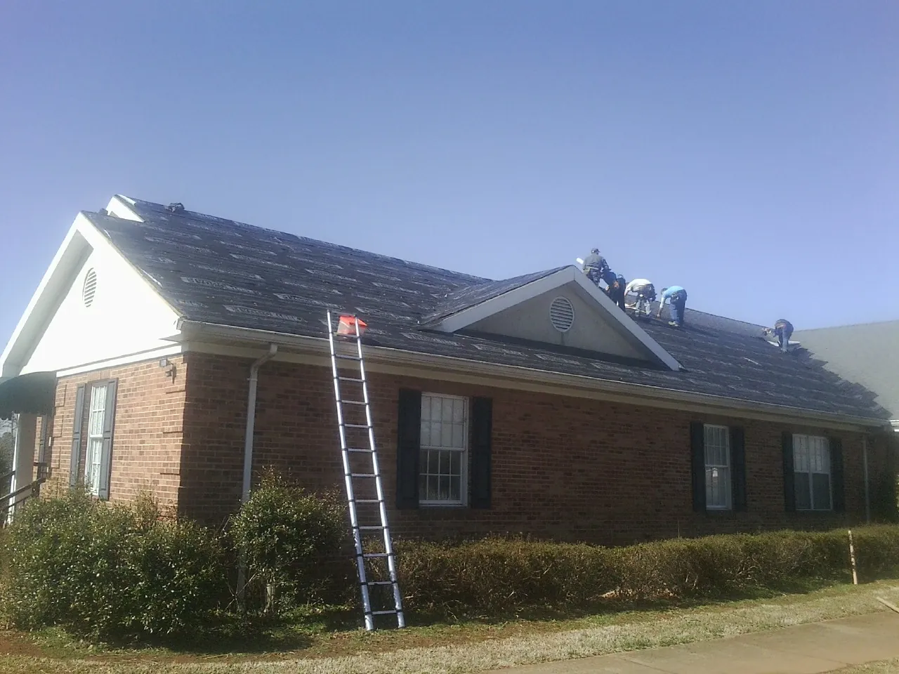 Crew tearing shingles off a brick ranch roof with a ladder set — Emergency Roof Repair work by our crew in New Berlin